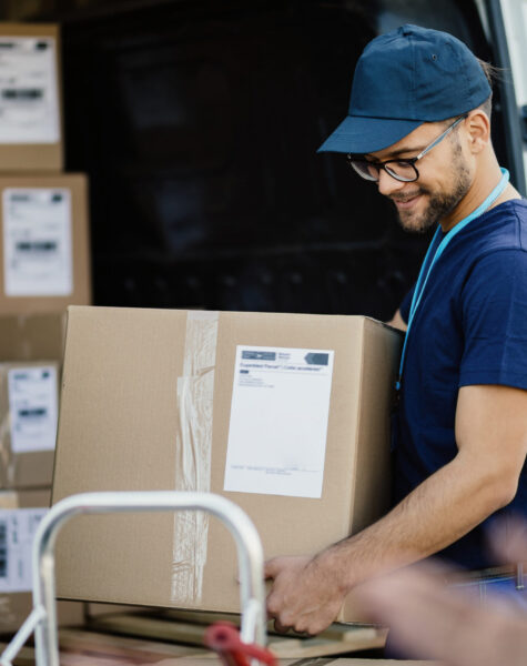 Young happy delivery man carrying cardboard box in a truck.