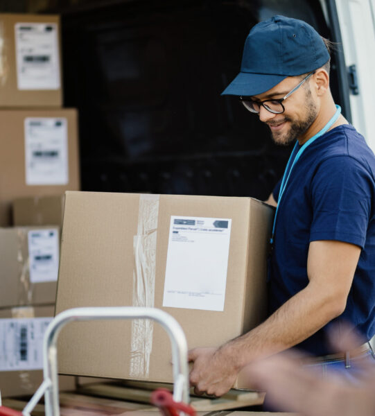 Young happy delivery man carrying cardboard box in a truck.